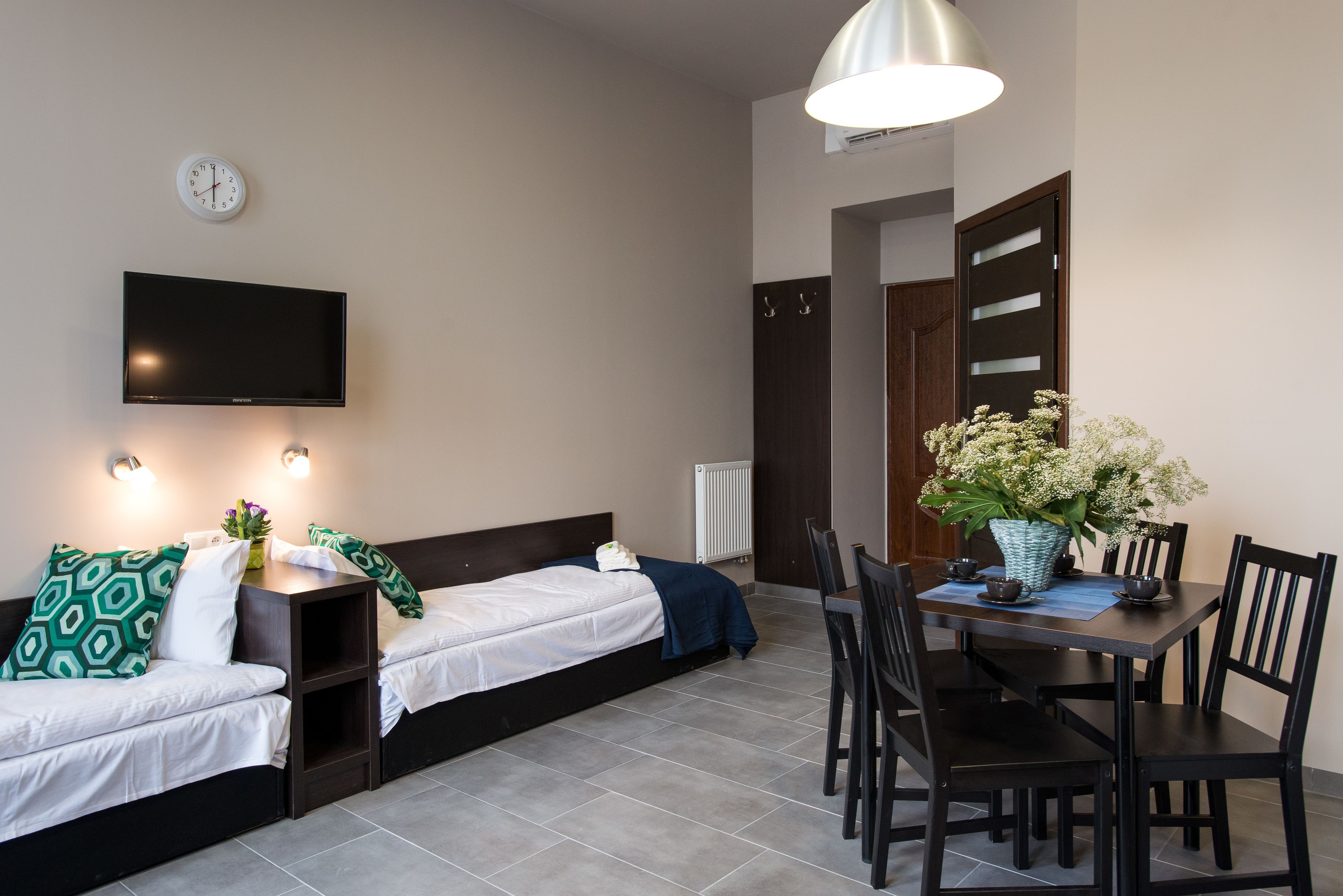 Ein modernes Zimmer mit einem Bett, einem Fernseher, einem Esstisch mit Stühlen und einer Topfpflanze.