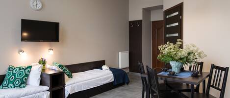 A modern room with a bed, a TV, a dining table with chairs, and a potted plant.