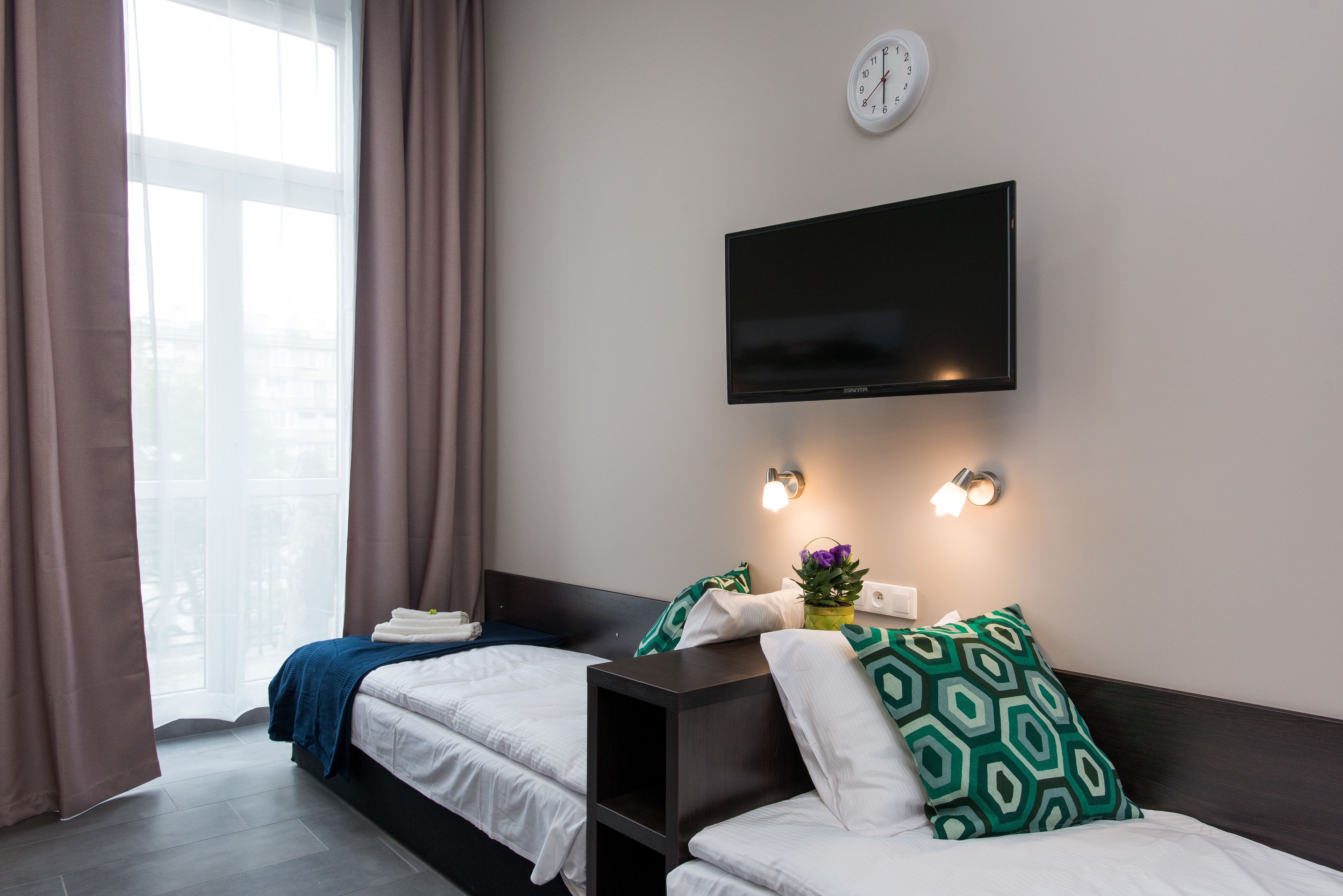 A hotel room with two beds, a TV mounted on the wall, and a window with curtains.