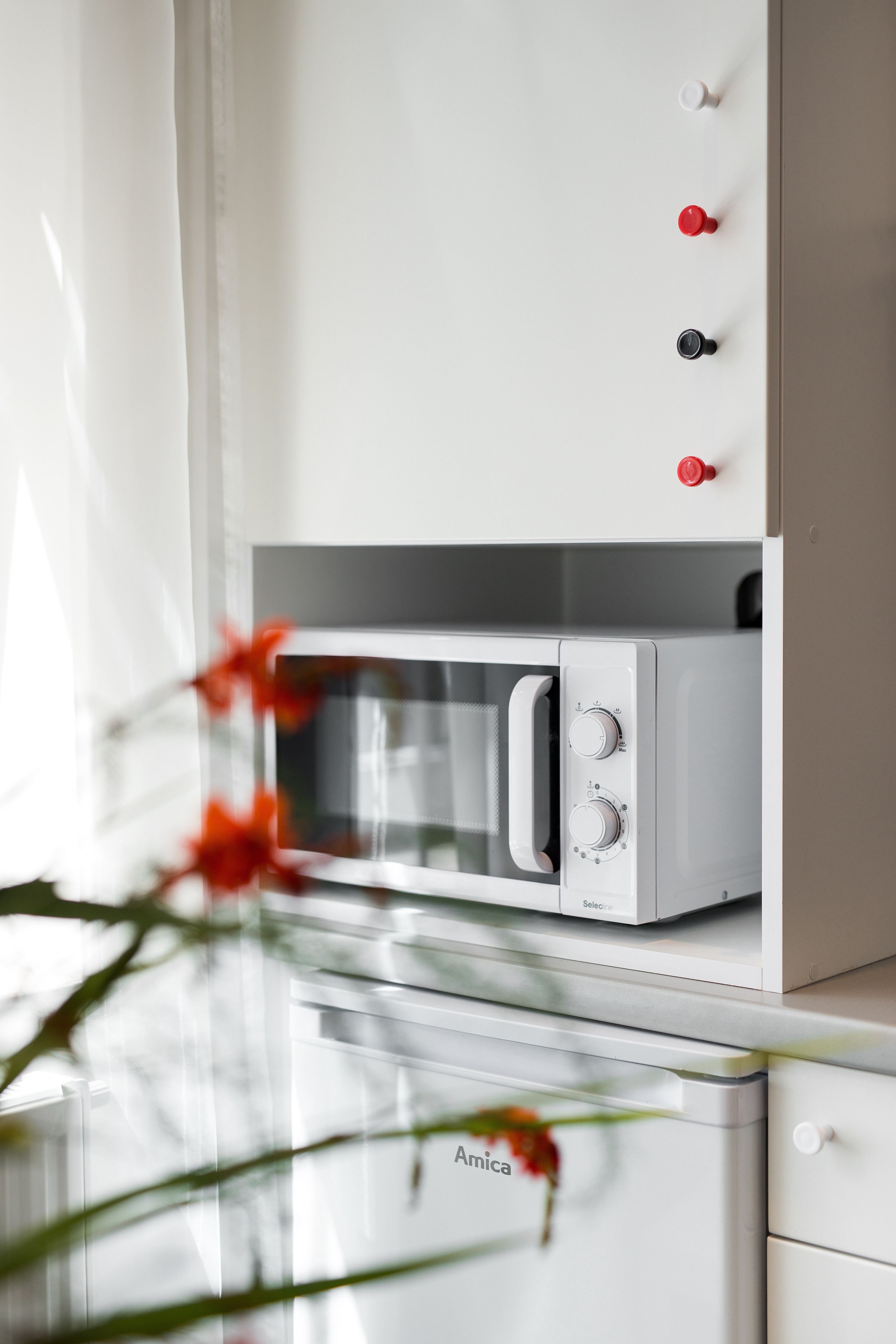 Un forno a microonde bianco con sportello in vetro, un pannello di controllo con due manopole e un pulsante rosso sul lato destro.