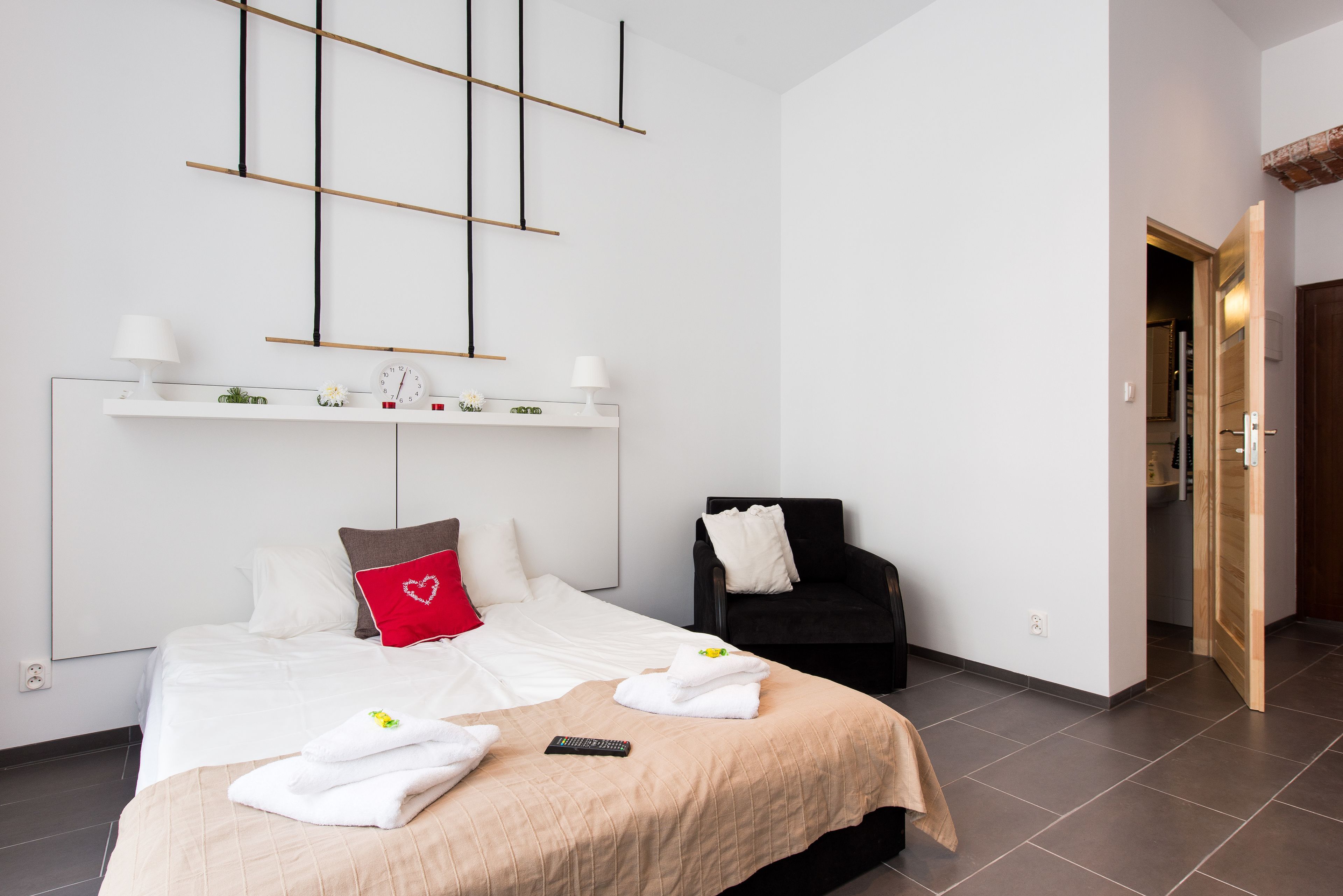 A modern hotel room with a large bed, a bedside table, a chair, and a wardrobe.