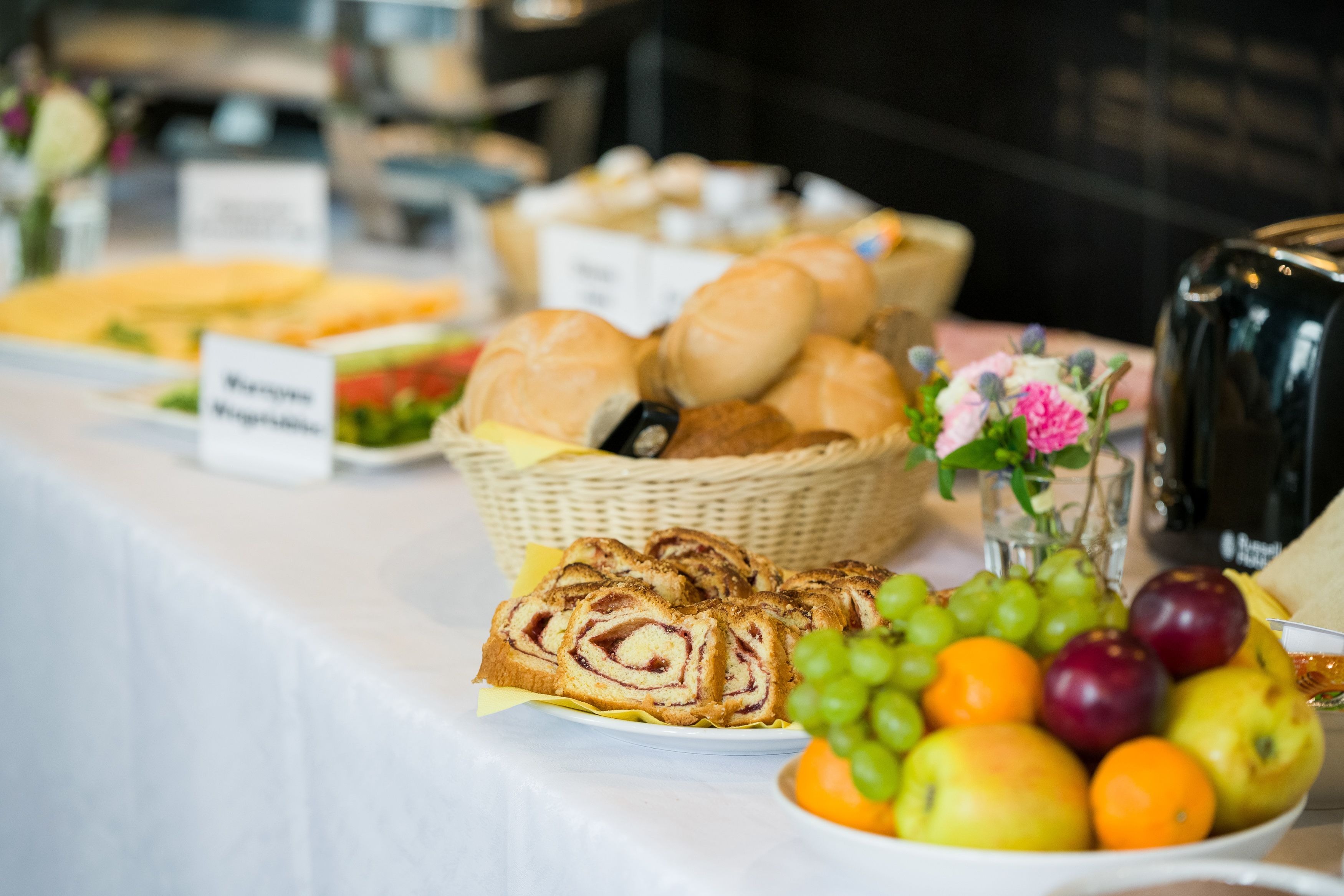 Une table de buffet proposant divers aliments, notamment du pain, des fruits, et un panneau indiquant les options végétariennes.
