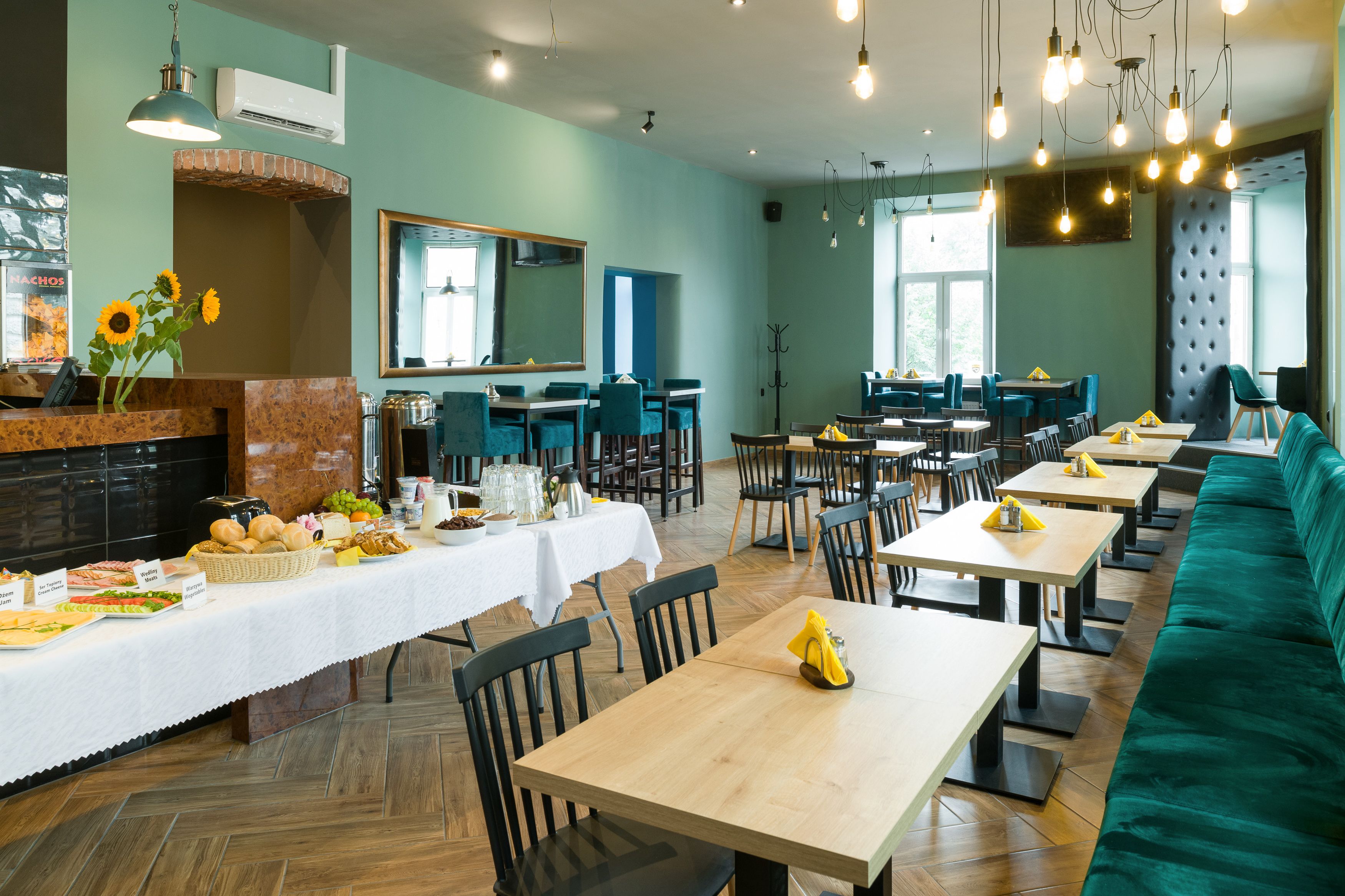 A restaurant with a long counter, multiple tables, and a green sofa.