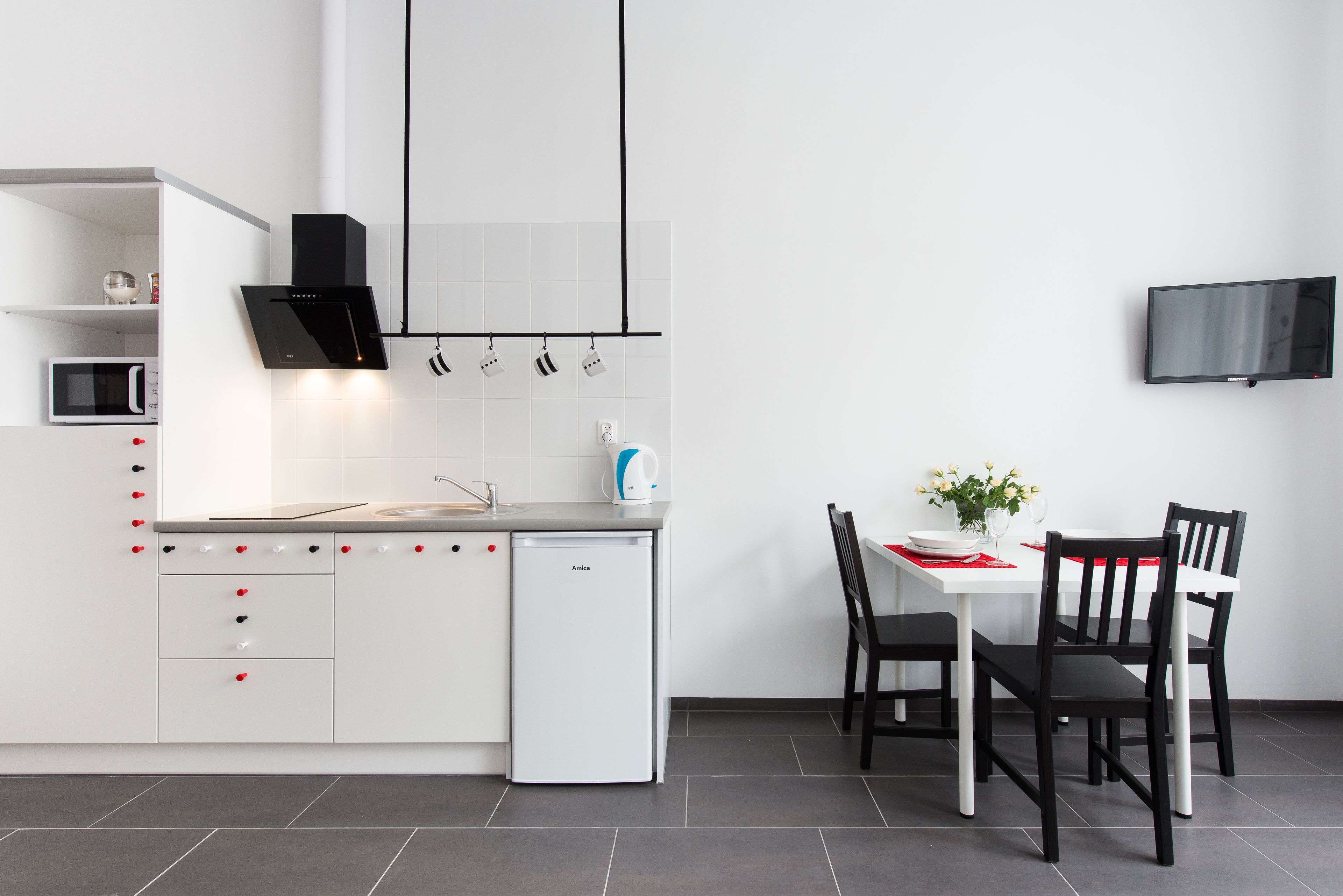 A modern kitchen with white cabinets, a built-in microwave, a dishwasher, and a dining area with a table and chairs.