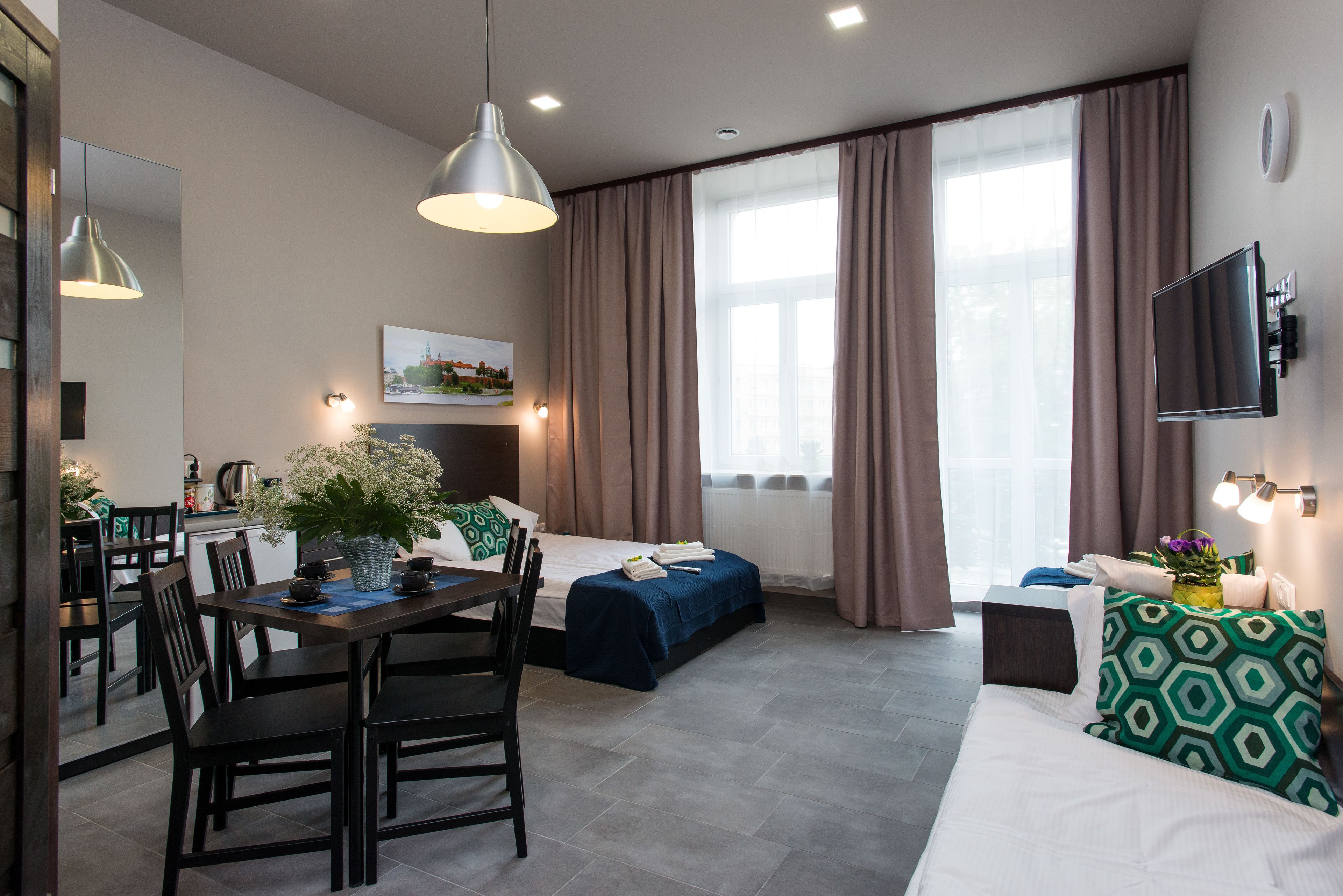 Una habitación de hotel moderna con zona de comedor, cama, sofá y televisor.
