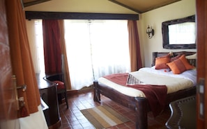 A bedroom with a wooden bed, red curtains, a wooden chair, and a window with a view. - Sangare Gardens (Mweiga)