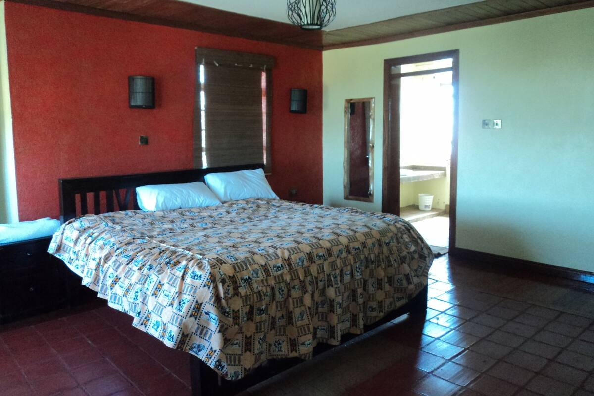 A bedroom with a bed, a window with blinds, a door, and a tiled floor.