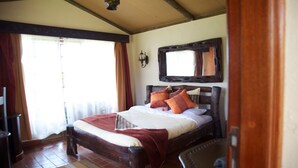 A bedroom with a wooden bed, a mirror above it, and a window with curtains. - Sangare Gardens (Mweiga)