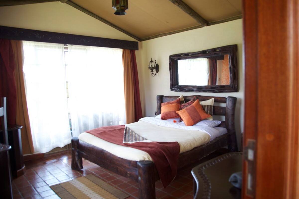 A bedroom with a wooden bed, a mirror above it, and a window with curtains.