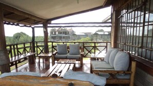 A wooden deck with a covered seating area, including a bench and two sofas with cushions. - Sangare Gardens (Mweiga)