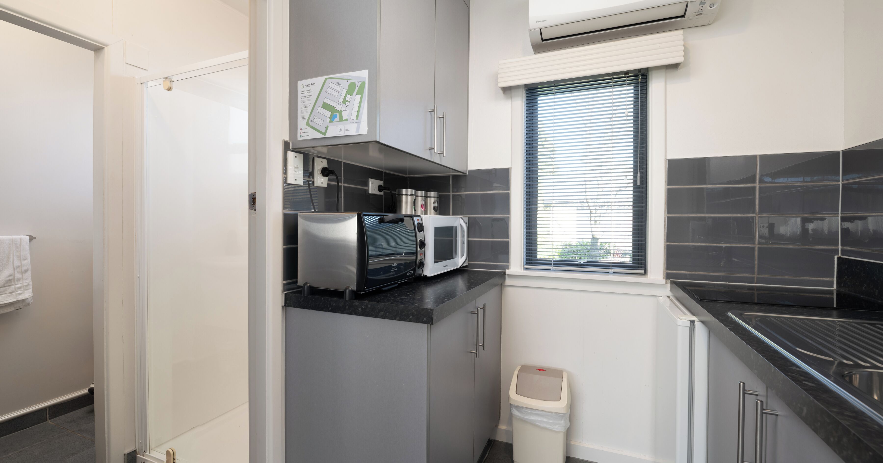 A compact kitchen with a microwave, toaster, and a trash bin.