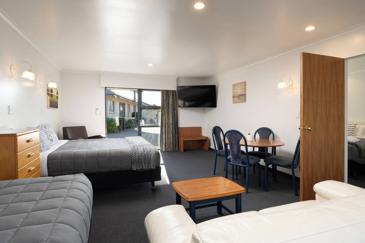 A hotel room with two beds, a desk, chairs, a TV, and a large mirror.