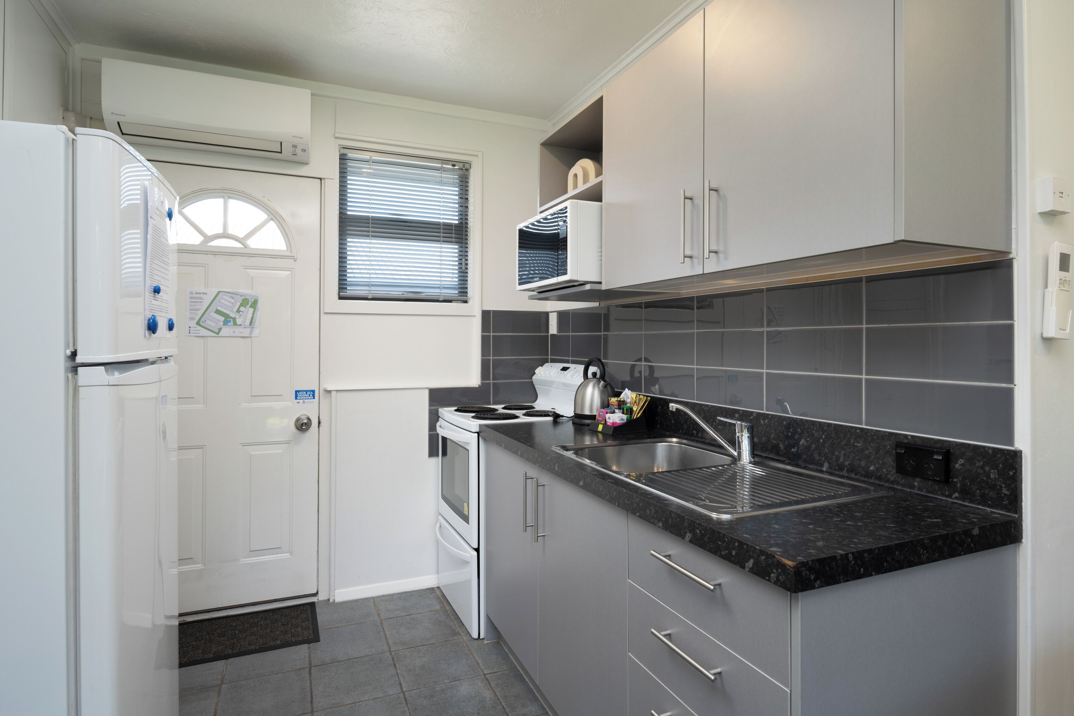 A compact kitchen with a refrigerator, stove, sink, and grey cabinets.