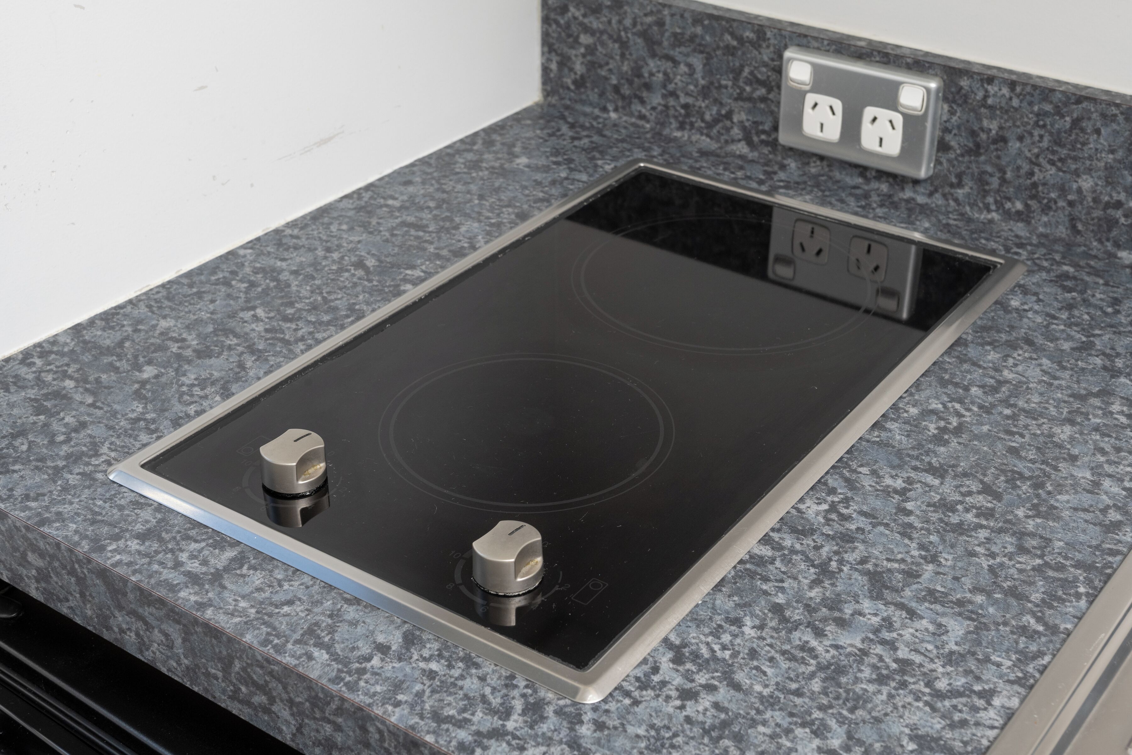 A kitchen with a black induction cooktop and two knobs, a granite countertop, and a double electrical outlet above the cooktop.