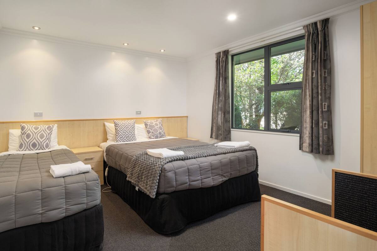 A hotel room with two beds, a large window with curtains, and a mirror on one wall.
