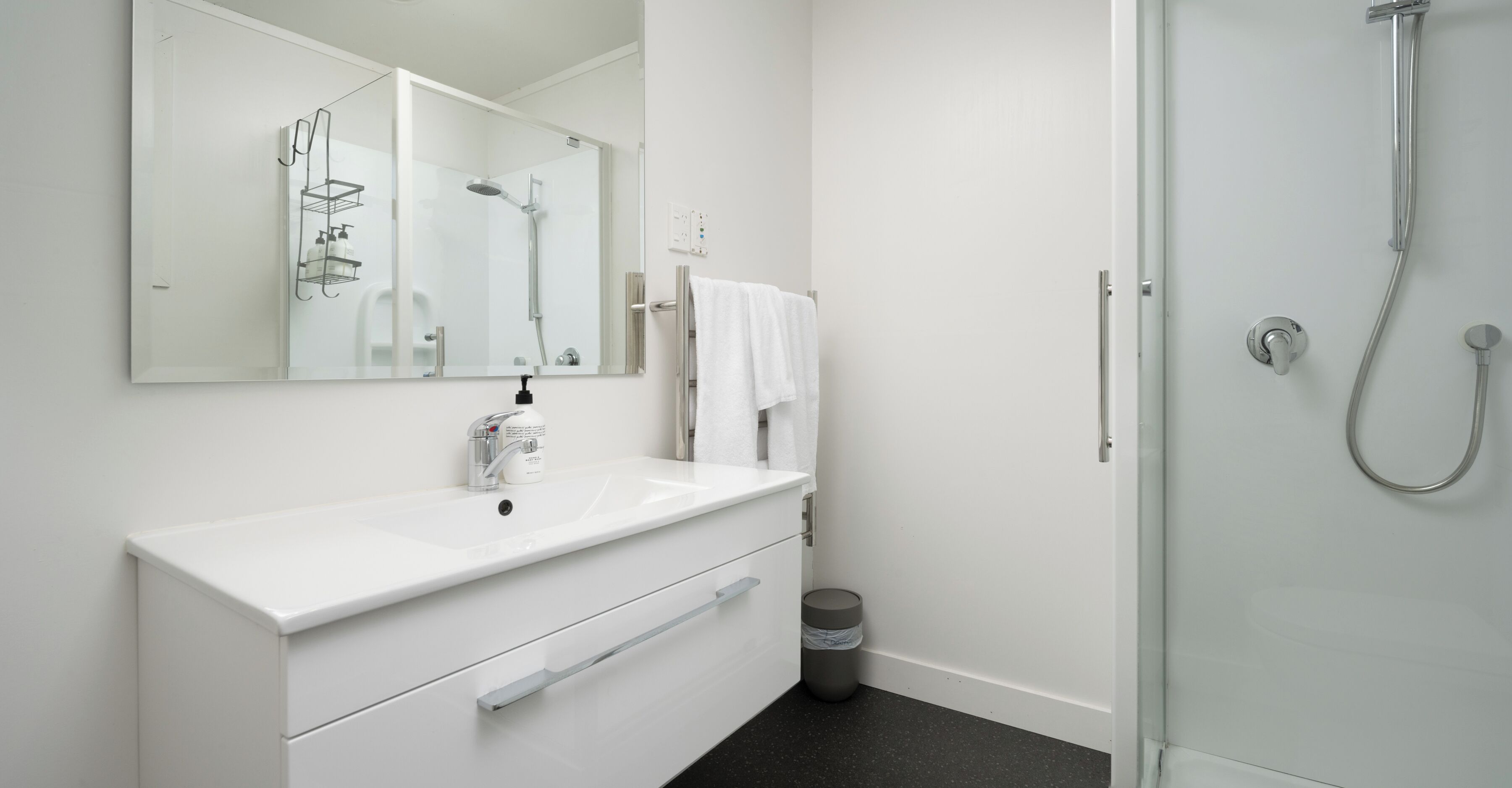 A modern bathroom with a white sink, mirror, and shower.