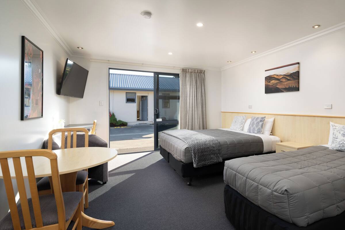 A hotel room with two beds, a desk, and a chair. There is a TV mounted on the wall and a window with curtains.