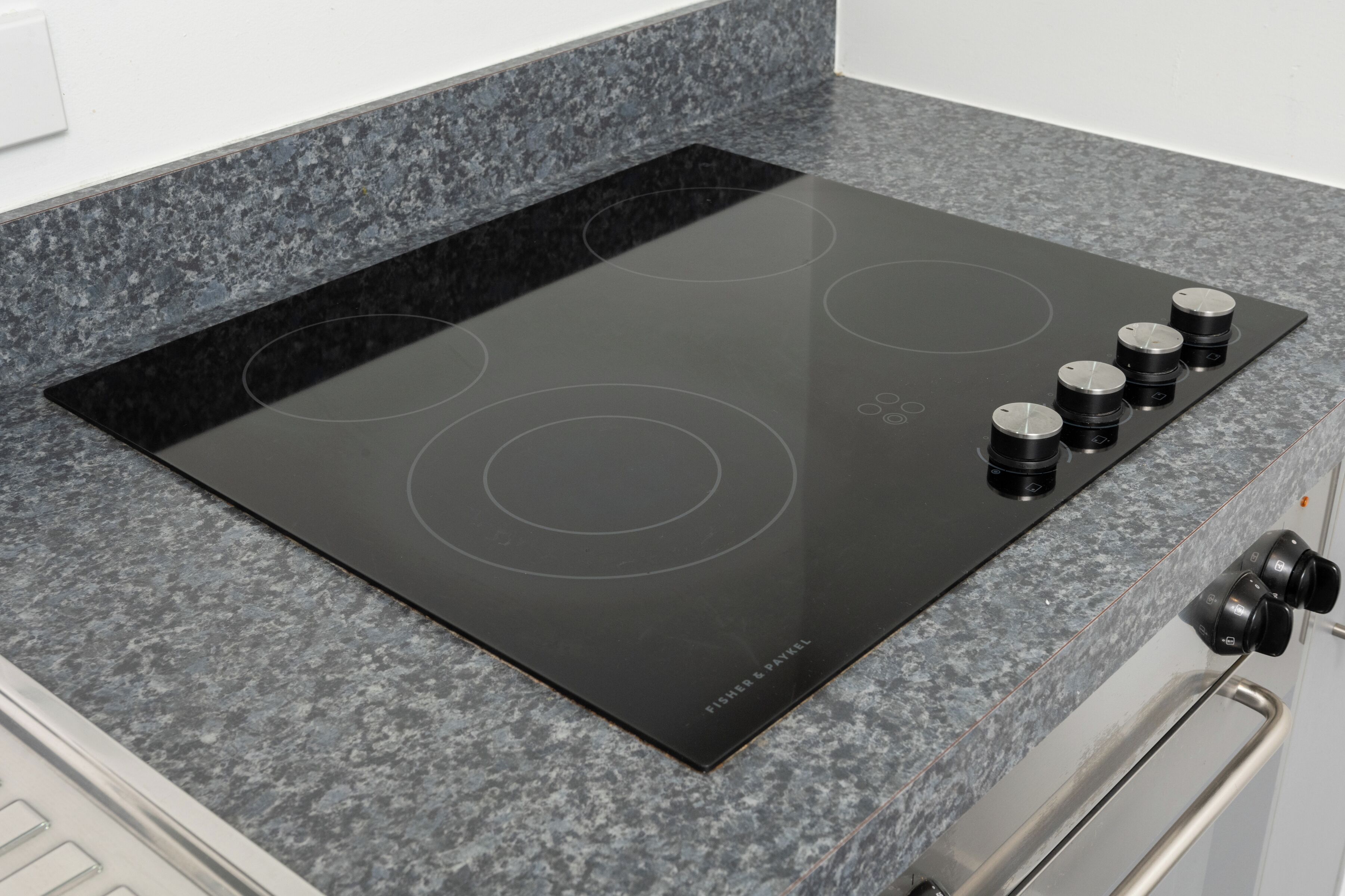 A black induction cooktop with four burners on a granite countertop.
