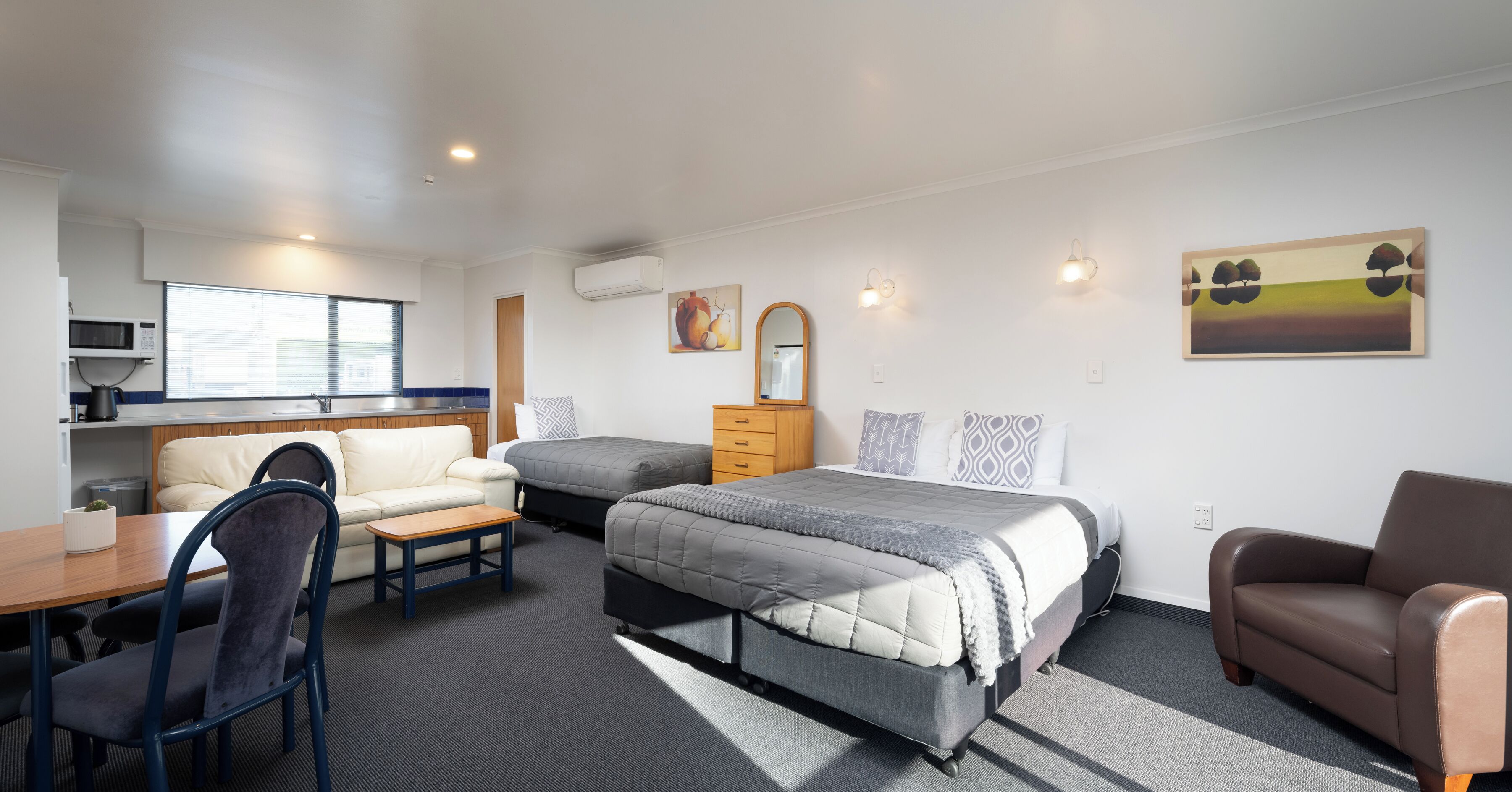 A compact hotel room with a kitchenette, a sofa, a bed, and a dining area.