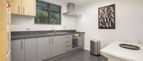 A modern kitchen with grey cabinets, a stainless steel sink, and a black trash bin.