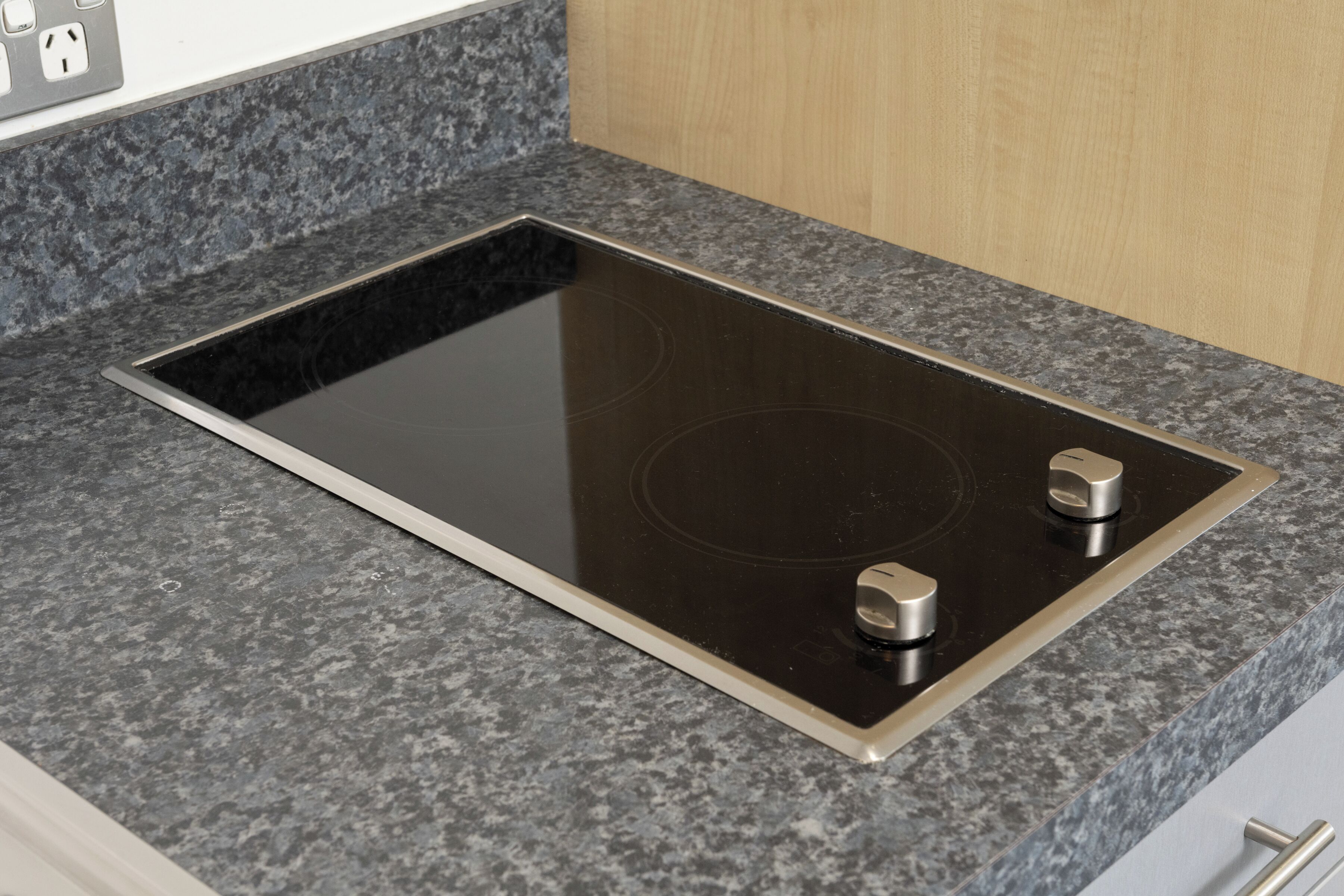 Una cocina con tope de inducción negro y dos perillas, encimera de granito y armarios de madera.