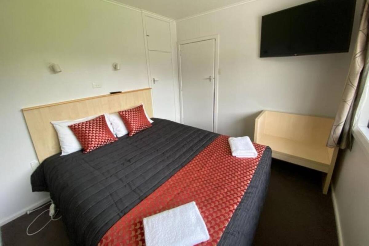 A hotel room with a bed, a TV mounted on the wall, and a door.