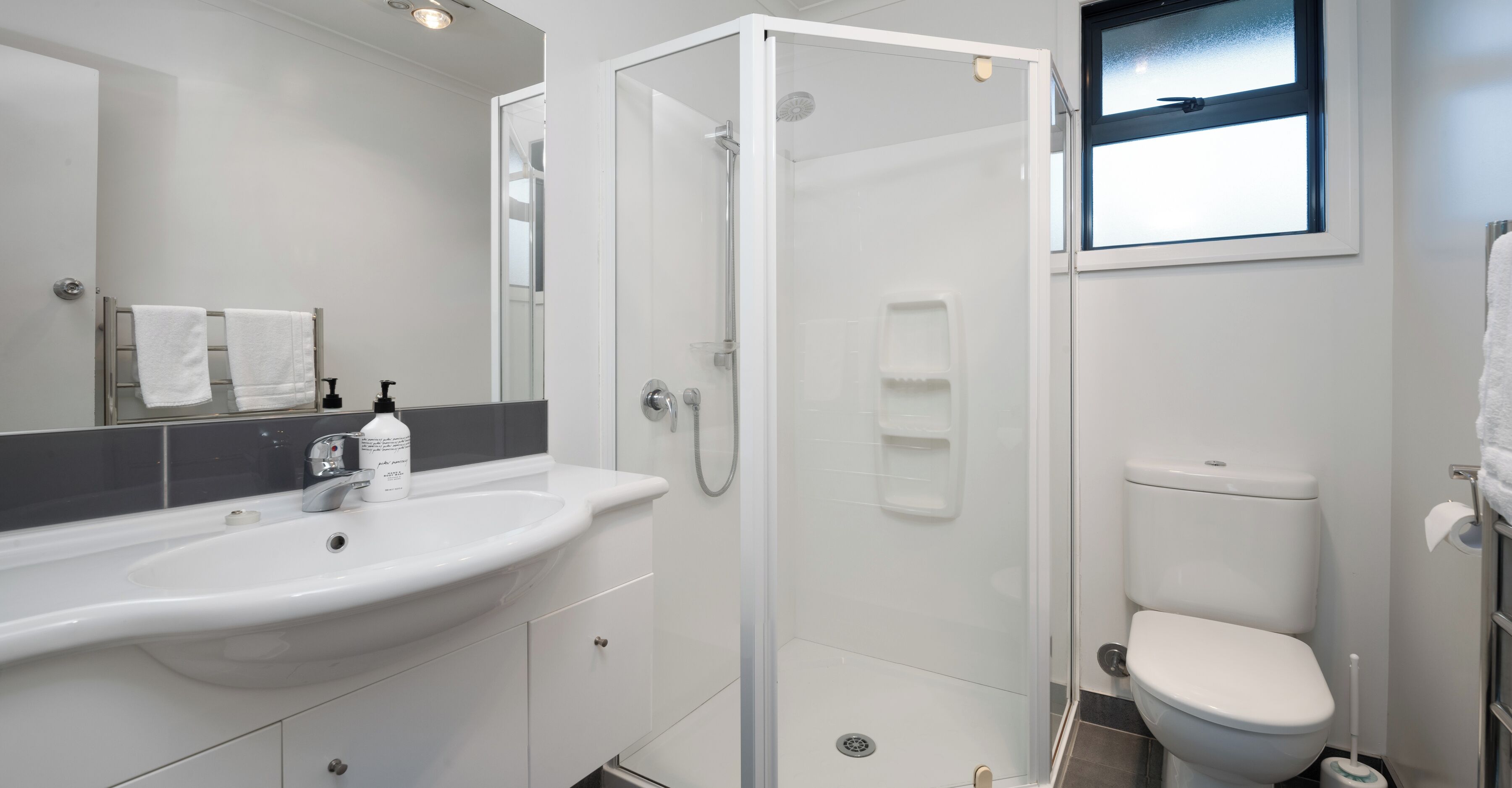 A modern bathroom with a glass-enclosed shower, a white sink, and a toilet.