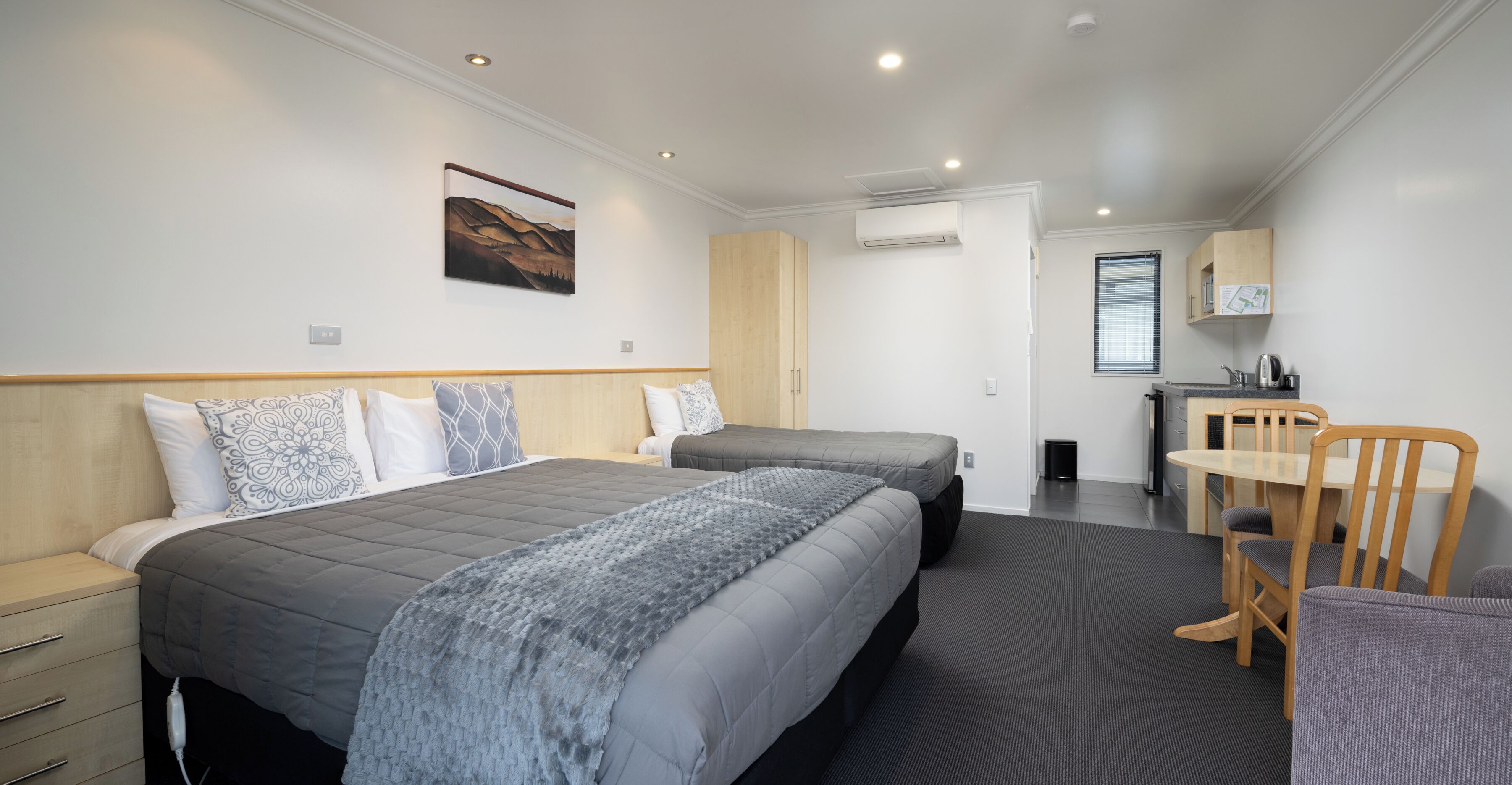 A modern hotel room with two beds, a desk, and a chair.