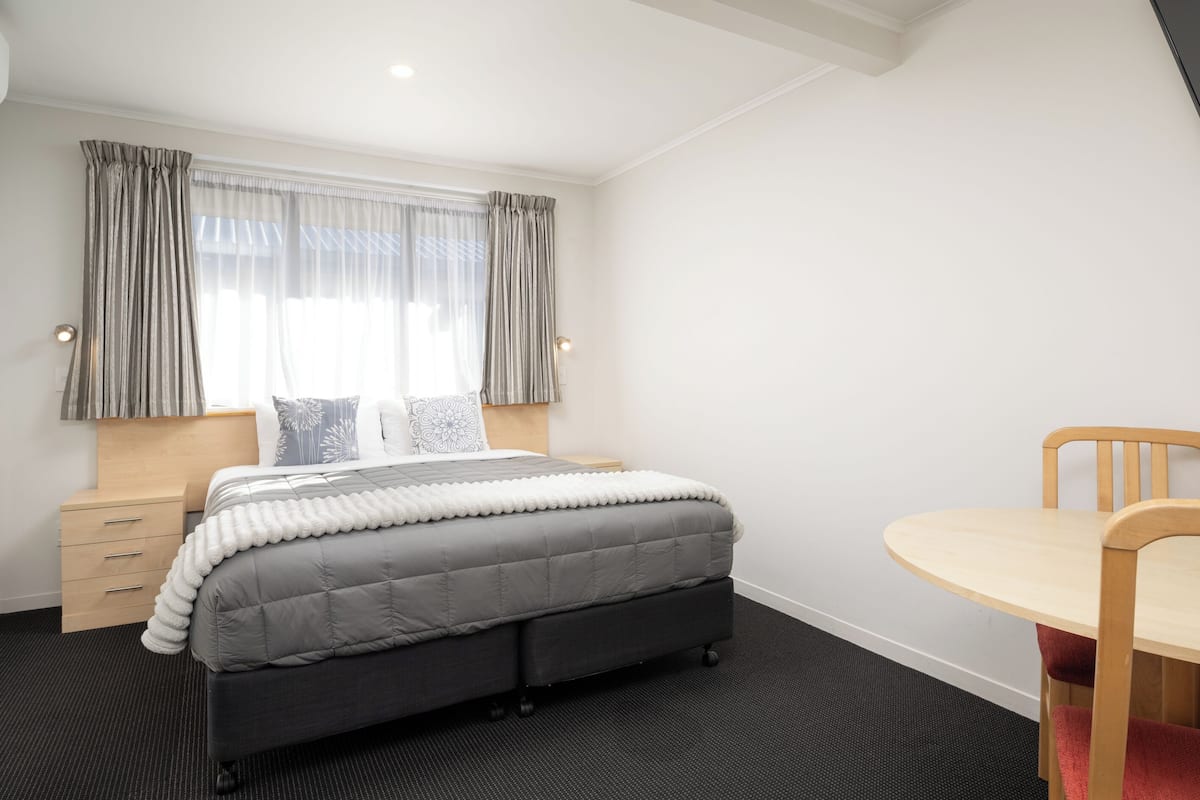 A neatly arranged bedroom with a bed, bedside table, and a small round table with a chair.