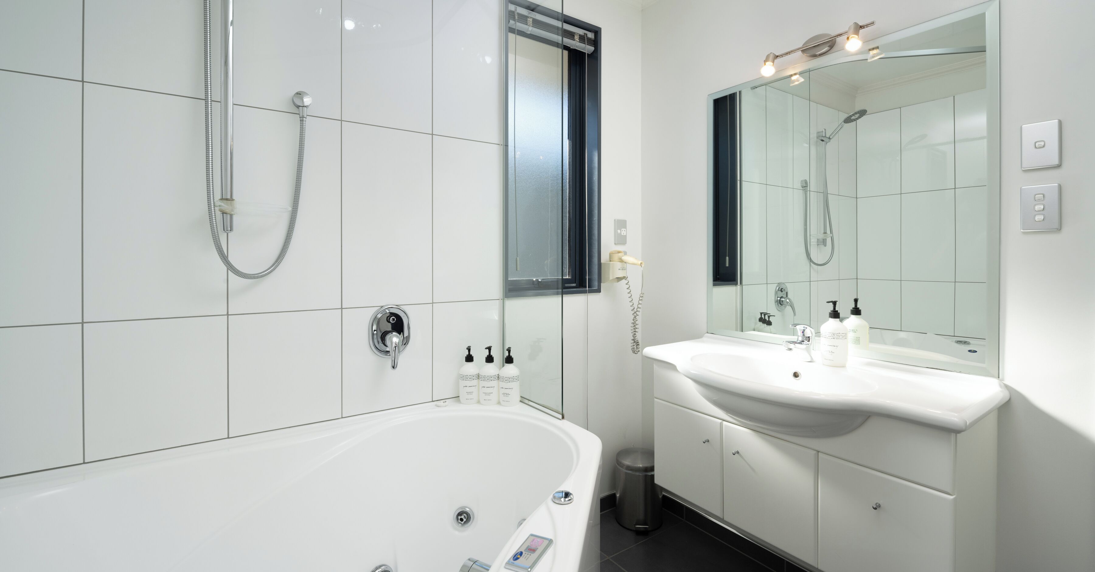 Un baño moderno con una bañera blanca, ducha con mampara de vidrio y tocador con espejo.
