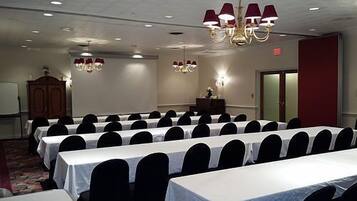 A conference room with rows of tables, a podium, and chandeliers.
