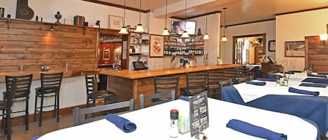Un restaurante con paredes de madera, una zona de bar y mesas con servilletas azules.