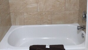 Un baño con bañera, paredes de azulejos y cabezal de ducha.