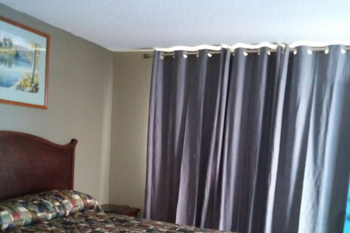 Une chambre à coucher avec un lit en bois, une couvre-lit à motifs, une fenêtre avec des rideaux et un tableau accroché au mur.