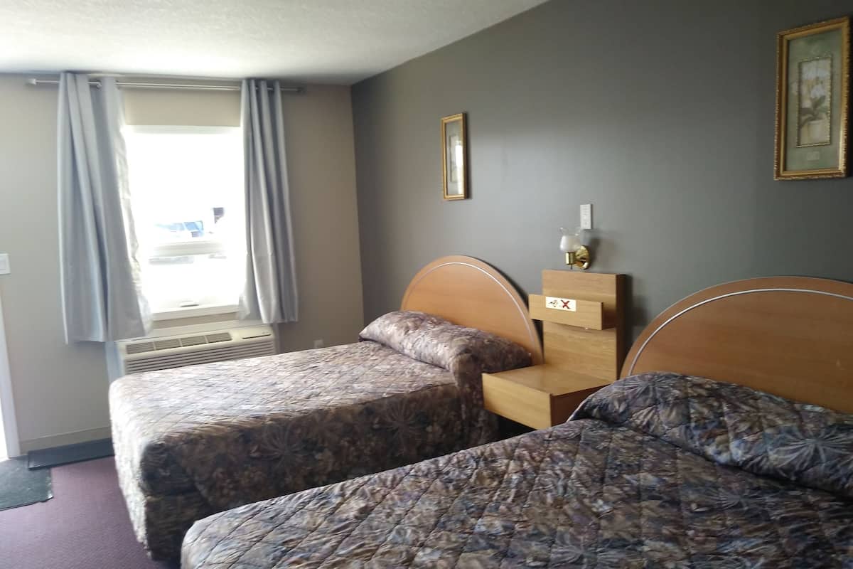 Une chambre d’hôtel avec deux lits, une fenêtre avec des rideaux, une lampe fixée au mur et un tableau encadré.
