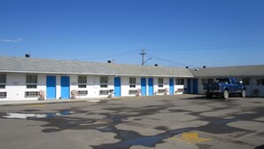 Un motel con una hilera de habitaciones, cada una con una puerta y una ventana azules. Un camión azul está estacionado frente al motel.