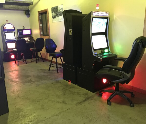 A gaming area with multiple arcade machines, chairs, and a large monitor.