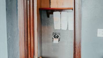 A wooden door leading to a bathroom with a toilet, a shelf with towels, and a tiled floor.