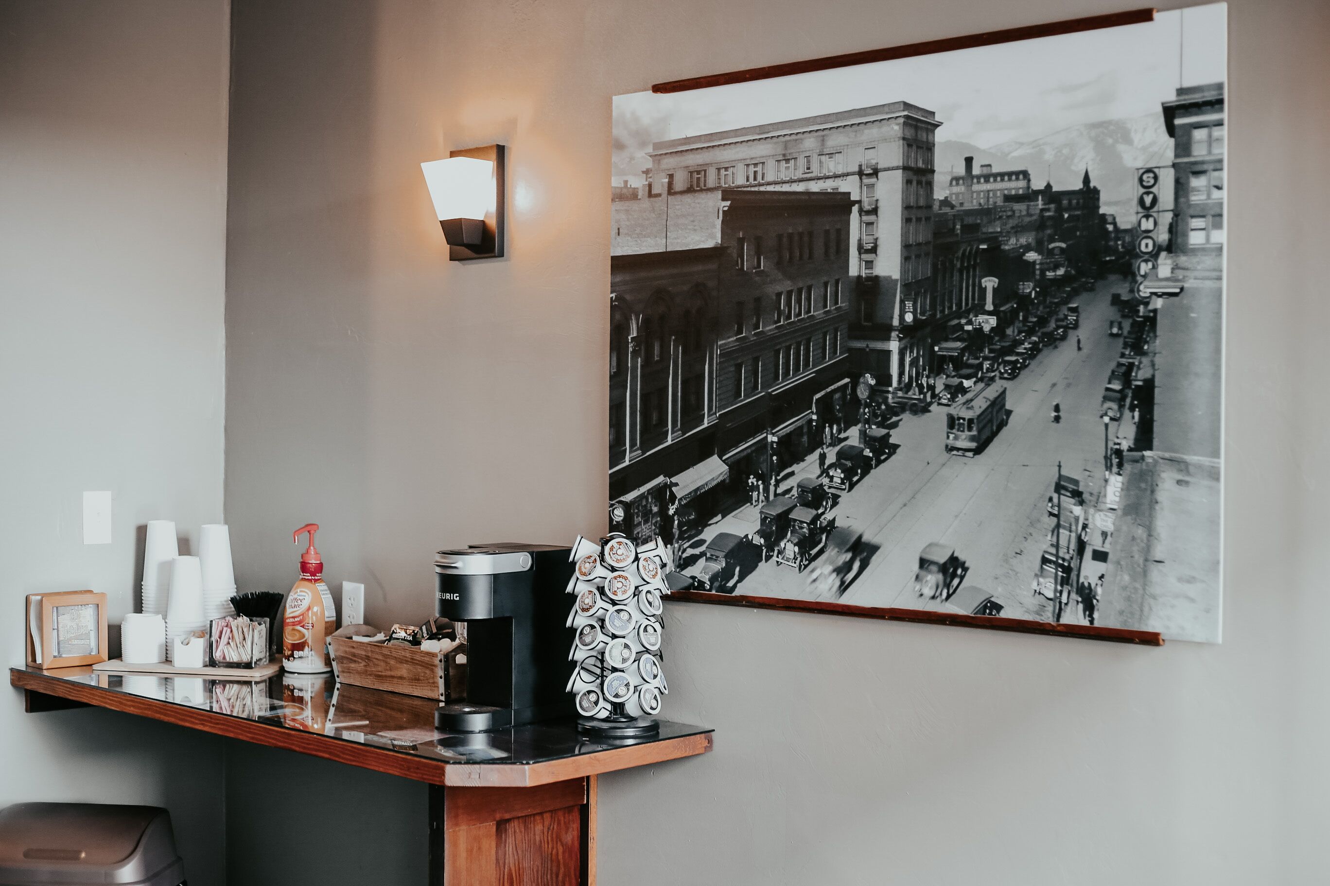 Una estación de café con una fotografía antigua de una escena callejera, una lámpara de pared y un cubo de basura.