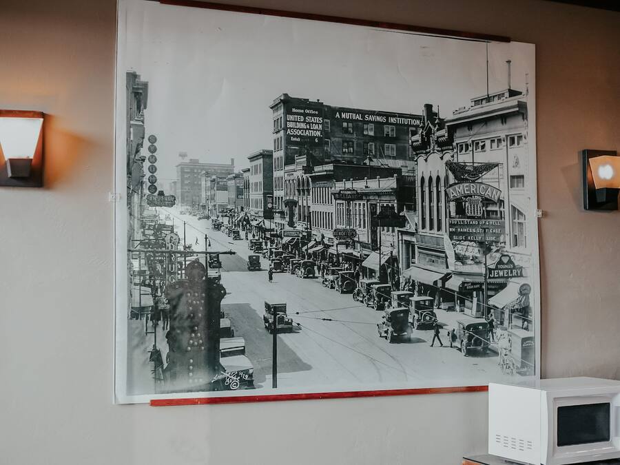 Zwart-wit foto van een levendige straat met oude auto's en gebouwen, waaronder een bord van een Wederzijds Spaarhuis.