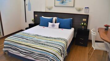 A neatly made bed with a striped bedspread, a headboard with two nightstands, a small table with a vase, and a chair.