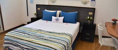A neatly made bed with a striped bedspread, a headboard with two nightstands, a small table with a vase, and a chair.