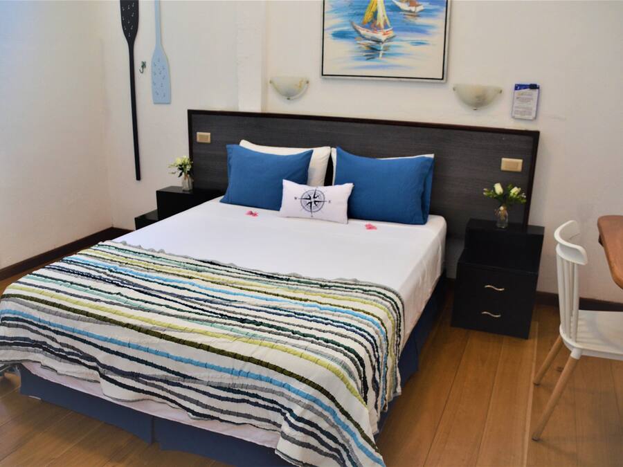 A neatly made bed with a striped bedspread, a headboard with two nightstands, a small table with a vase, and a chair.