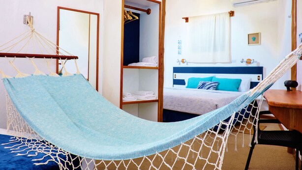 A room with a hammock, a bed with a blue headboard, a bedside table, a mirror, and a wardrobe. - Capitan Max B&B (Puerto Ayora)