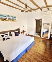Un dormitorio con una cama grande, vigas de madera en el techo, un cuadro de pájaros, una mesita con un jarrón y un espejo que refleja la habitación.