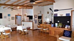 A dining area with wooden tables and chairs, a bar area with a counter and stools, and a kitchen in the background. - Capitan Max B&B (Puerto Ayora)