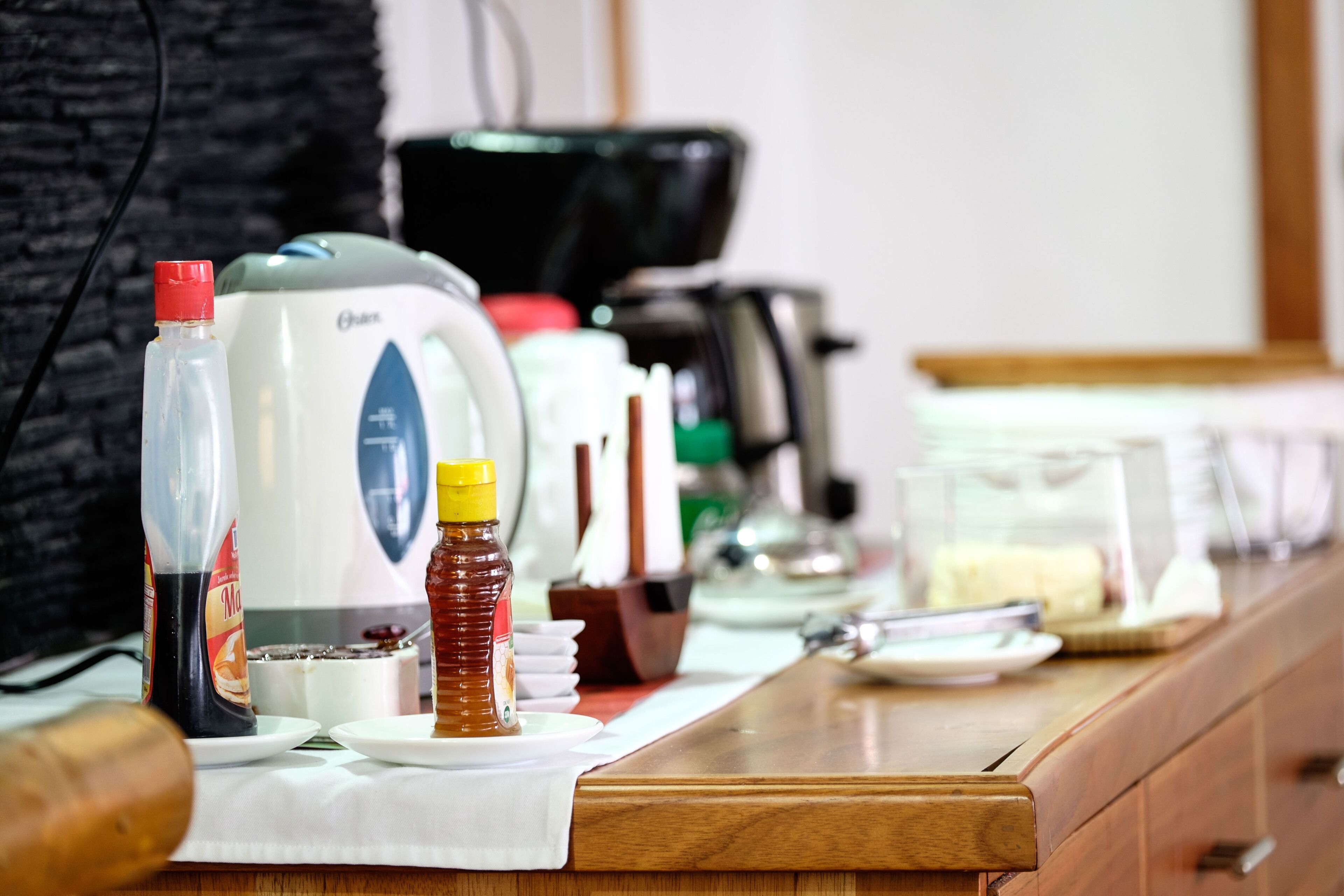 A kitchen counter with a coffee maker, a bottle of honey, and a jar of jam.