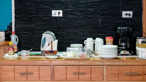 A kitchen counter with various appliances and items, including a kettle, coffee maker, and stacked plates. - Capitan Max B&B (Puerto Ayora)