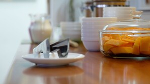 A breakfast buffet with a glass container of sliced fruit, a plate with a spoon, and stacked bowls in the background. - Capitan Max B&B (Puerto Ayora)