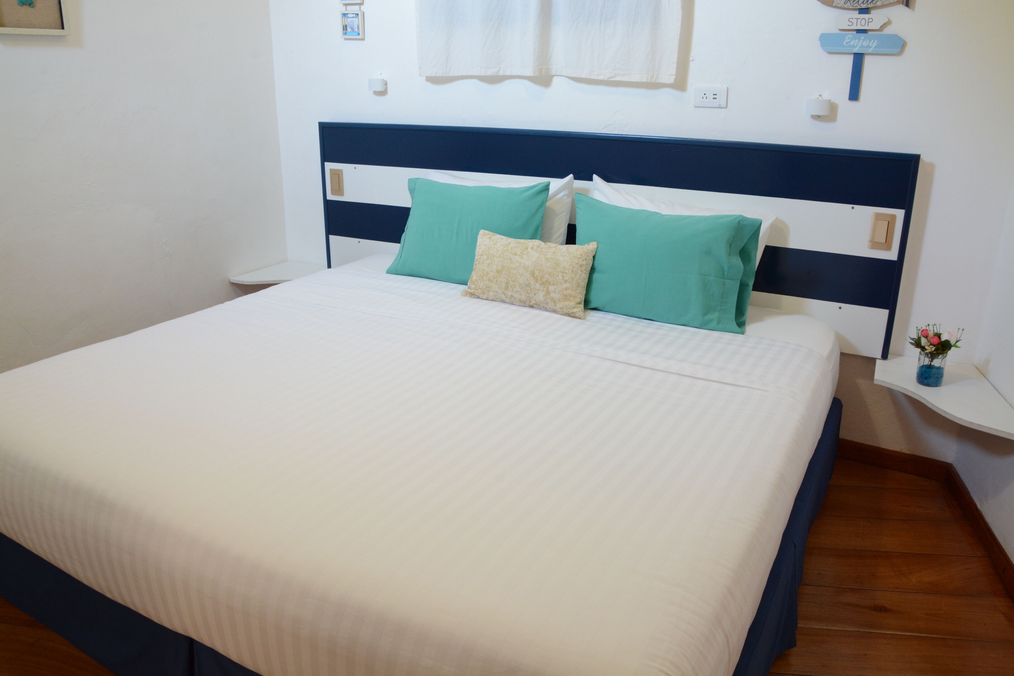 Una cama bien hecha con un cabecero blanco y azul, dos almohadas color turquesa y una almohada decorativa color beige.